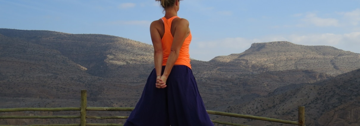 Frau macht Yogaübung auf einer Holzplattform mit Bergpanorama im Hintergrund